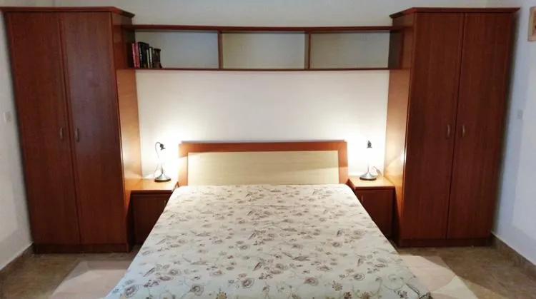 Bedroom featuring a double bed, wooden wardrobes on both sides, and a shelf above the headboard.