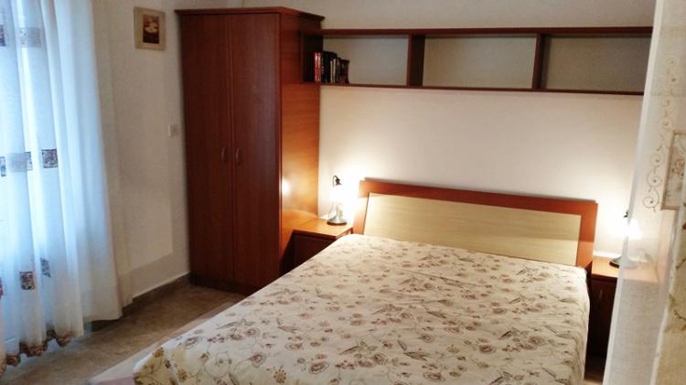 Cozy bedroom in a hotel in Budva, Montenegro: double bed, wooden wardrobe, bedside tables and shelves.