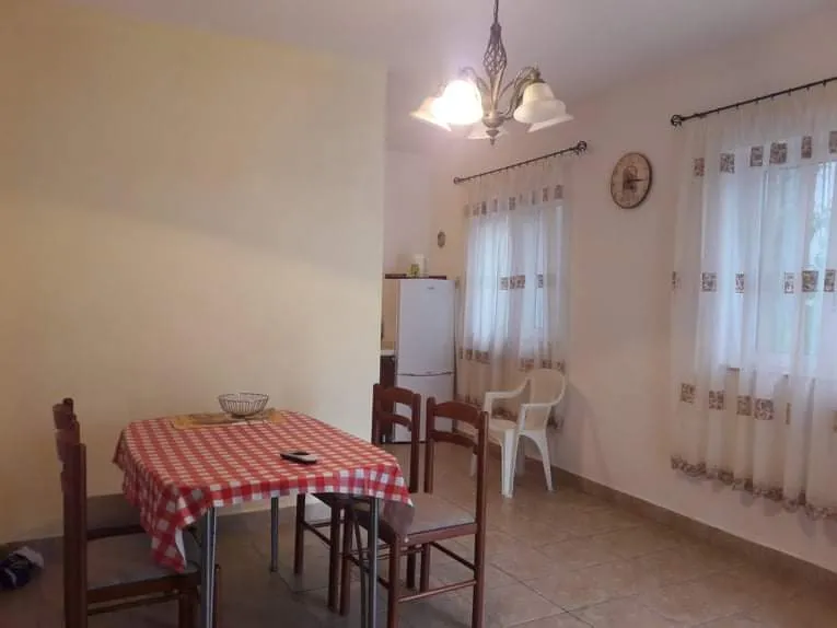 Dining area with a red and white checkered tablecloth, wooden chairs, and a white refrigerator visible in the background.