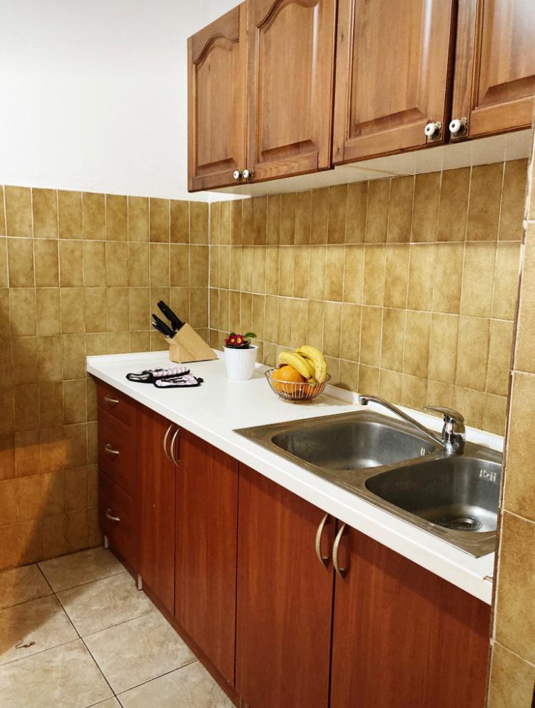 Hotel kitchen in Budva, Montenegro: wooden cabinets, white countertop, stainless steel sink, and tiled backsplash.