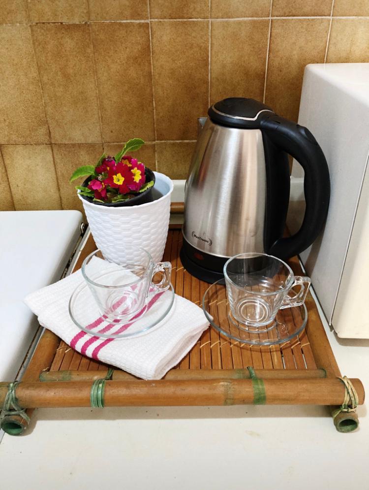 Kitchen nook in a hotel in Budva, Montenegro: electric kettle, glass cups on a bamboo tray, and floral decor.