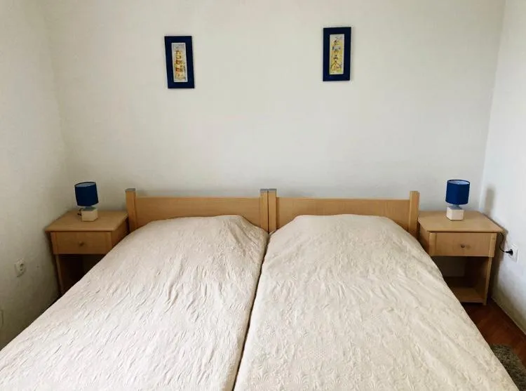 Two single beds with white covers, wooden nightstands, and blue lamps against a plain white wall.