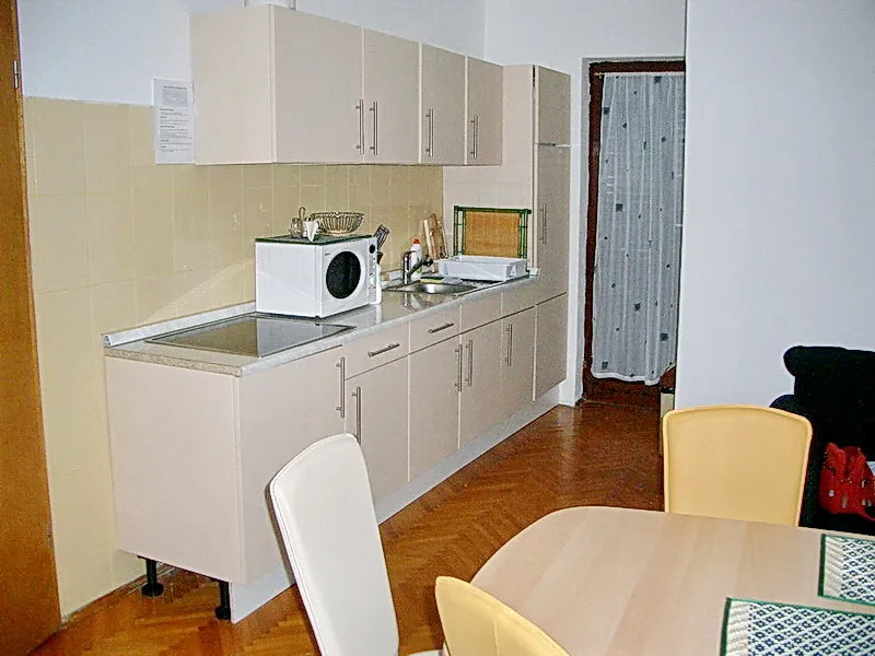 Kitchen with beige cabinets, microwave, sink, and dining table on parquet flooring.