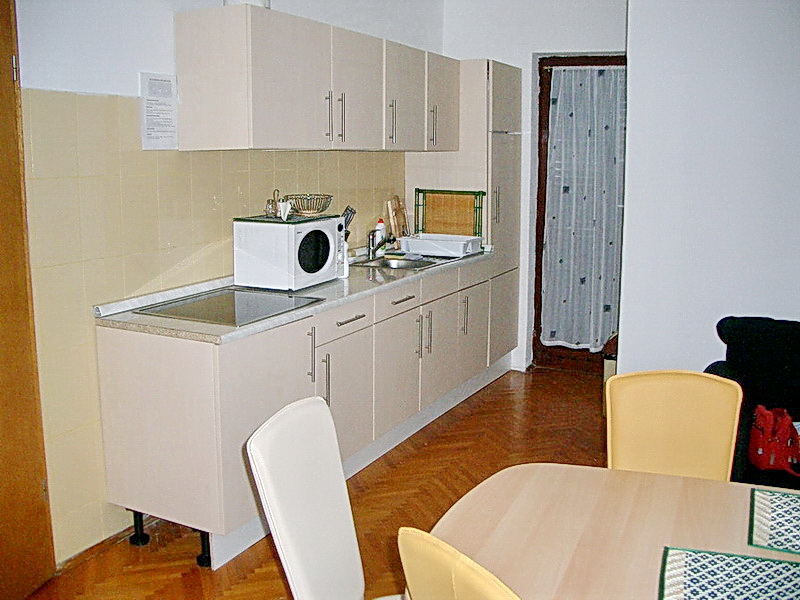 Hotel kitchen in Budva, Montenegro: light-colored cabinetry, dining area, parquet floor, and access to the balcony.