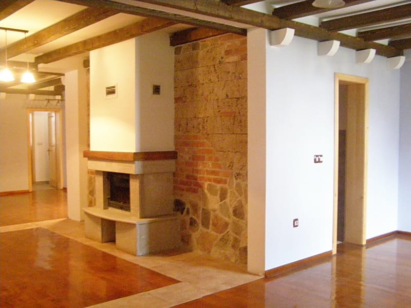 Villa living room in Stoliv, Montenegro: interior with a fireplace, stonework, wooden beams, and a glossy floor.