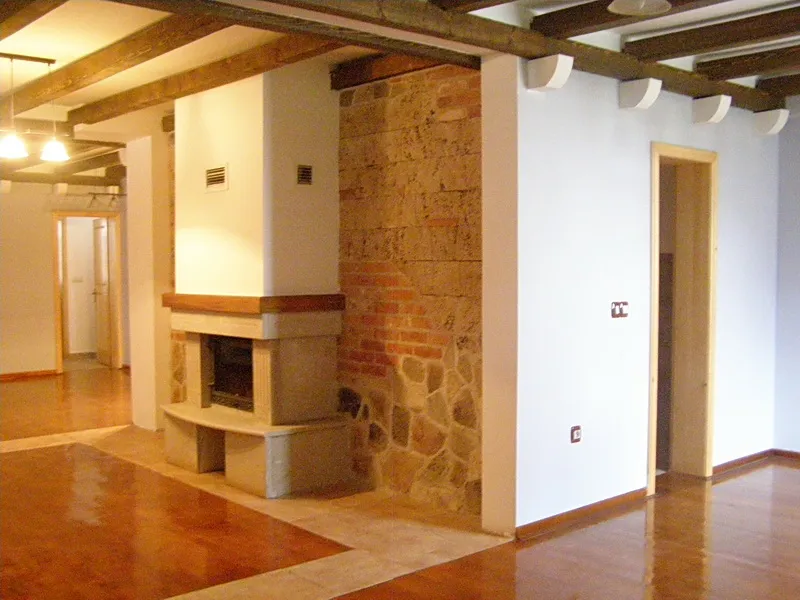 Empty room featuring a central fireplace, exposed wooden ceiling beams, and polished parquet flooring.