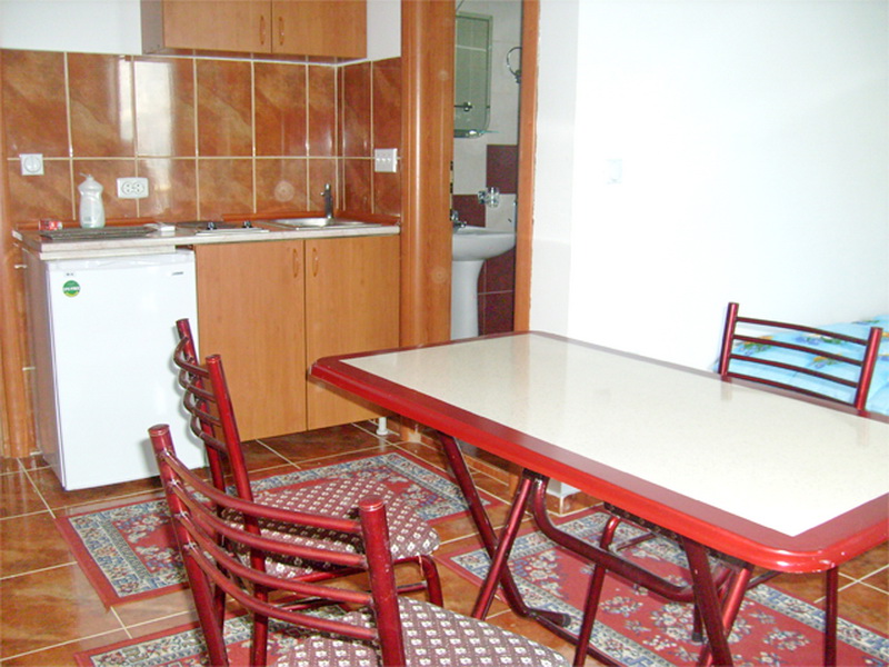 Kitchen with dining area in a villa in Prčanj, Montenegro: wooden cabinets, tiled floor, table with chairs, and a view of the bathroom.