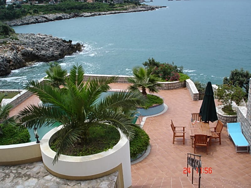 Villa terrace in Utjeha, Montenegro: pool, palm trees, wooden furniture, and panoramic views of the Adriatic Sea.