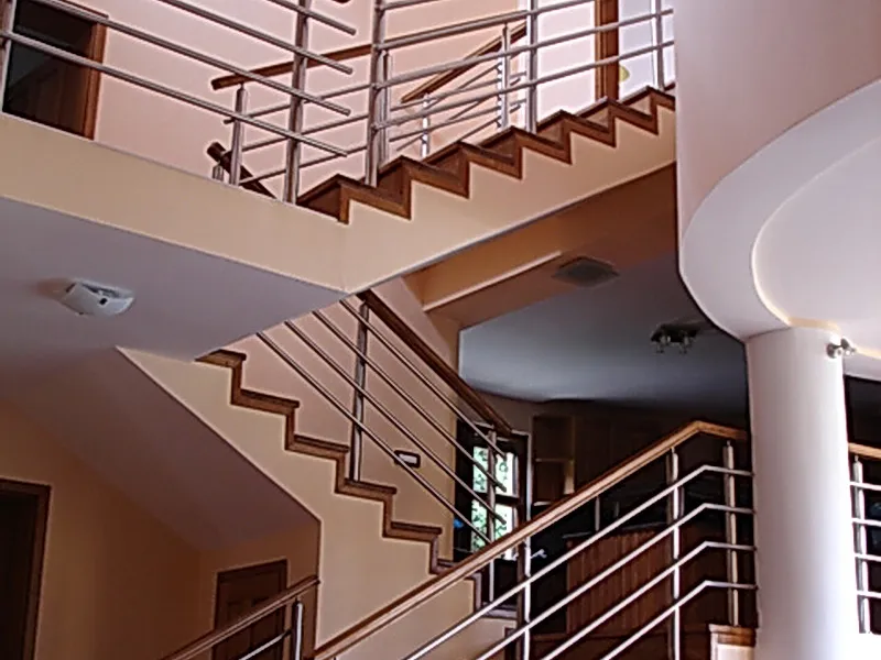 Interior staircase with wooden steps and metal railings, featuring a white column and ceiling lights in a multi-level space.