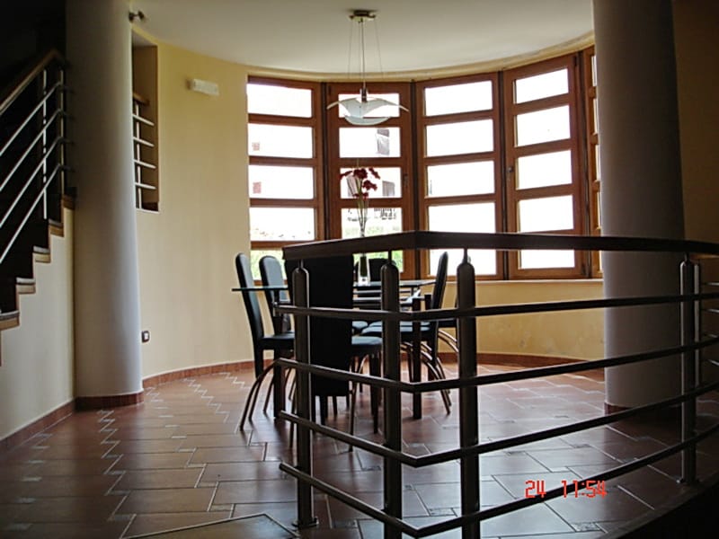 Living room with dining area and panoramic windows in a villa in Utjeha, Montenegro: tiled floor, columns, and staircase.