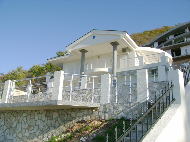 White villa with a terrace and stone facade in Bar, Montenegro: view of the house with stairs and columns.