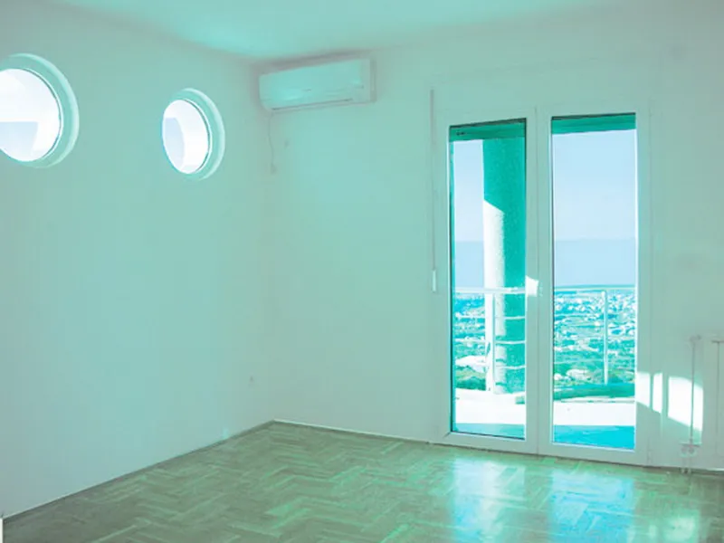 Empty room with parquet flooring, round windows, and a glass door leading to a balcony overlooking the sea.