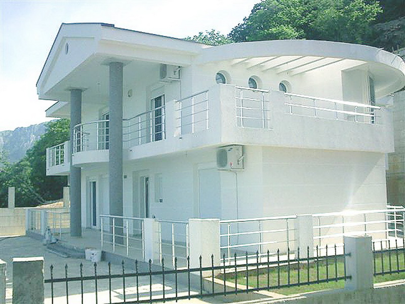 Two-story white villa in a modern style with terraces and columns in Bar, Montenegro. Front view of the house.