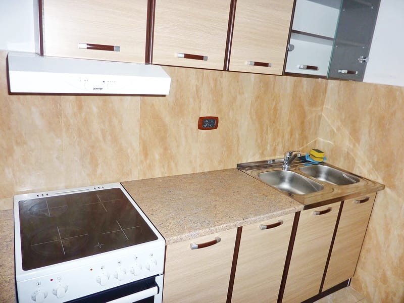 Kitchen in an apartment in Rafailovici, Montenegro: light-colored cabinets, electric stove, range hood, and stainless steel sink.