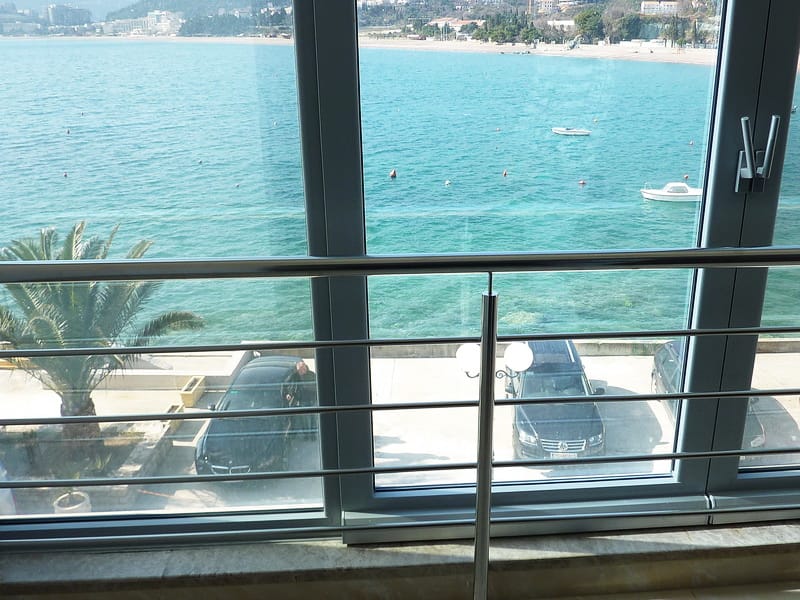 Sea and beach view from the apartment balcony in Rafailovici, Montenegro: panoramic windows, metal railings, and parking.