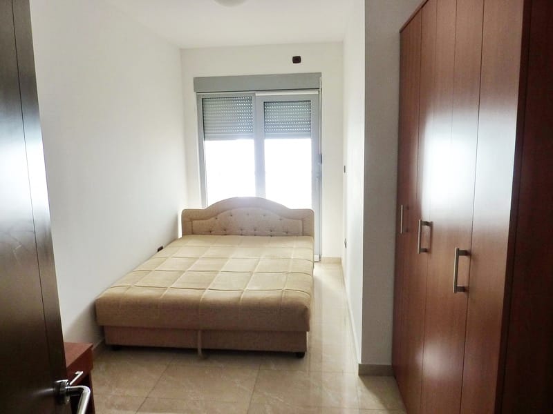 Bedroom in an apartment in Rafailovici, Montenegro: double bed, built-in wardrobe, and access to the balcony with roller shutters.