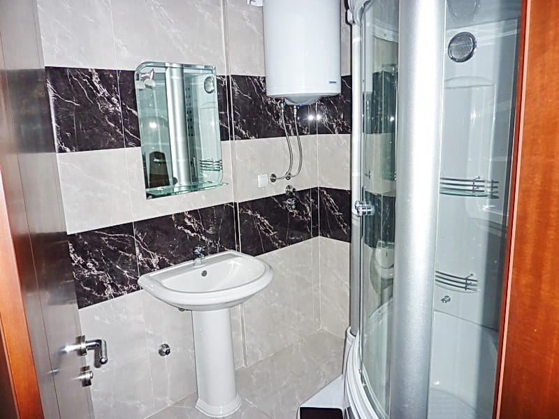 Bathroom in an apartment, Rafailovici, Montenegro: shower cabin, sink and water heater, tiled interior finish.