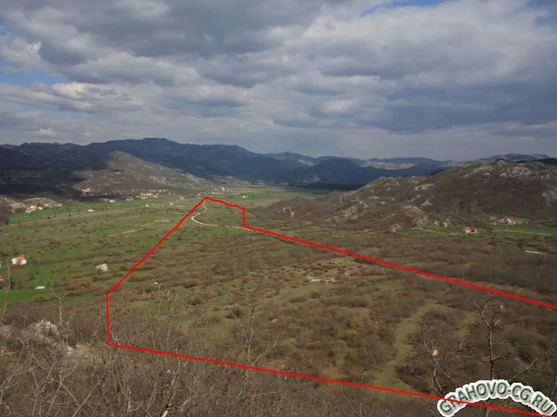 Panoramic view of a mountainous landscape with a red plot boundary line, green fields, and distant village.