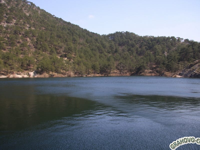 A picturesque mountain lake on a plot of land in Grahovo, Nikšić, Montenegro, surrounded by dense coniferous forest.