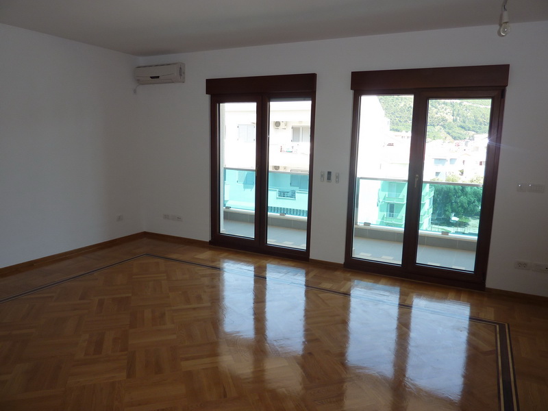 Bright living room with parquet flooring and access to the balcony in an apartment in Budva, Montenegro. City and mountain view.