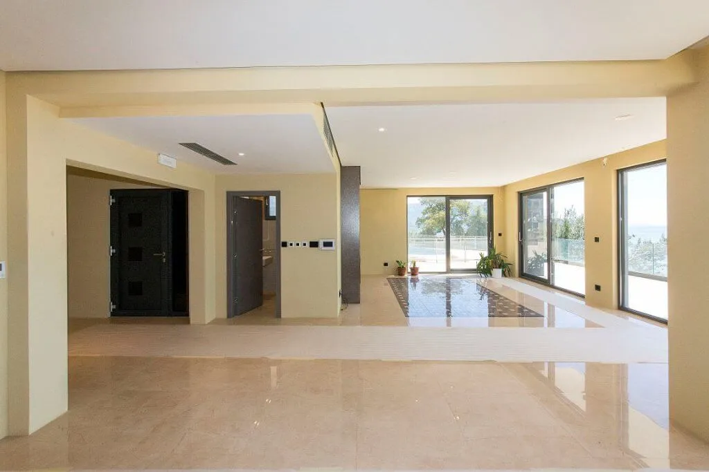 Large empty room with glossy tiled floors, panoramic windows, and a main entrance door.