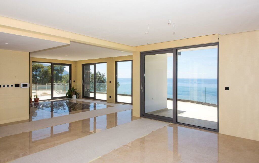 Spacious living room in a villa in Budva, Montenegro, with panoramic windows, marble flooring, and direct sea views.
