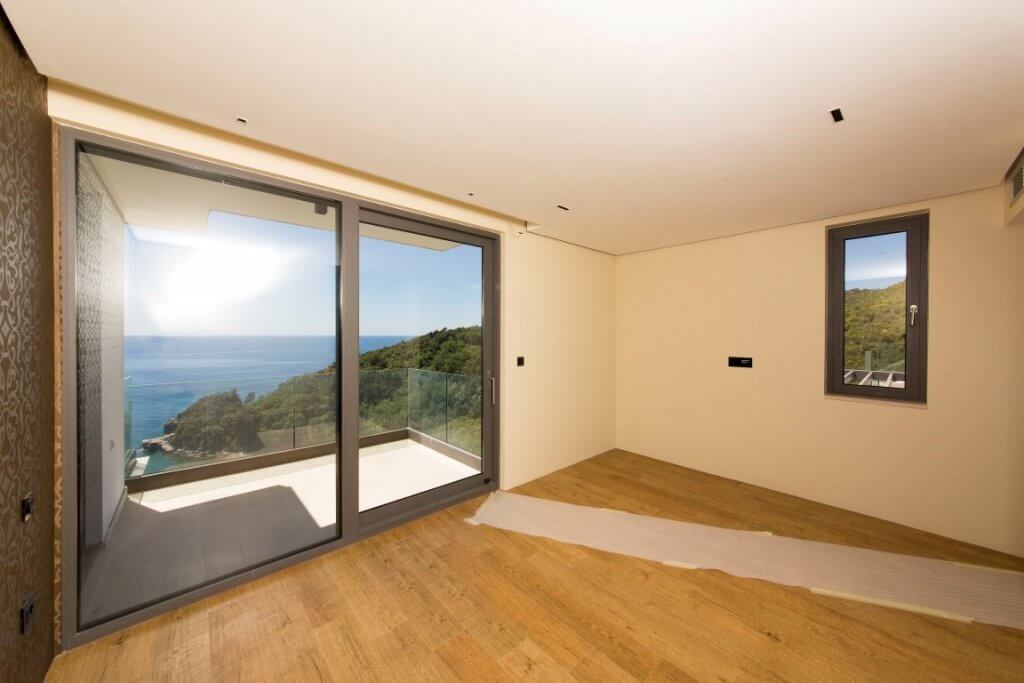 Bedroom in a villa in Budva, Montenegro: panoramic window with sea view, terrace, and bright interior finishes.