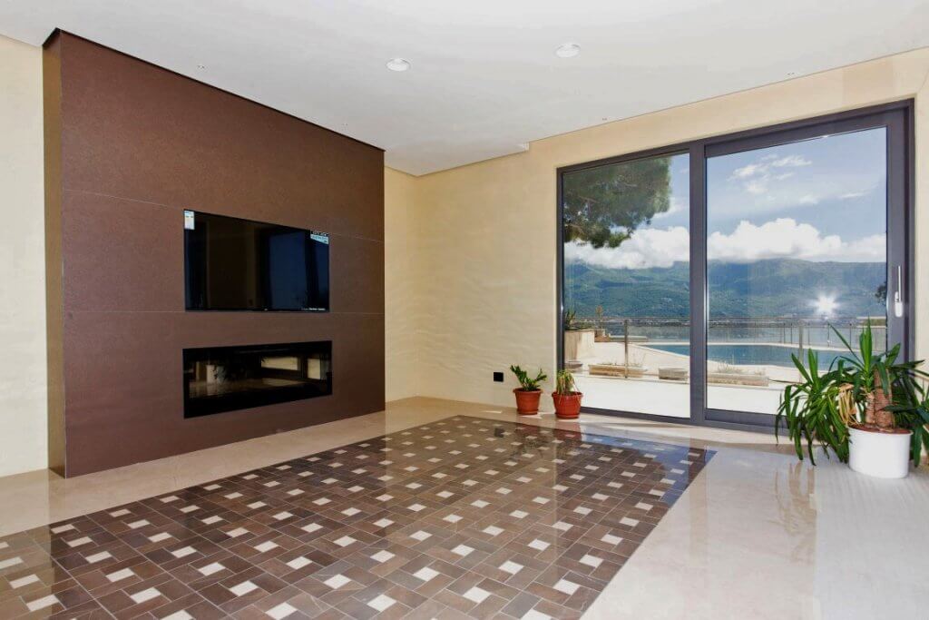 Villa living room in Budva, Montenegro: panoramic windows, sea view, modern fireplace, and stylish tiled flooring.