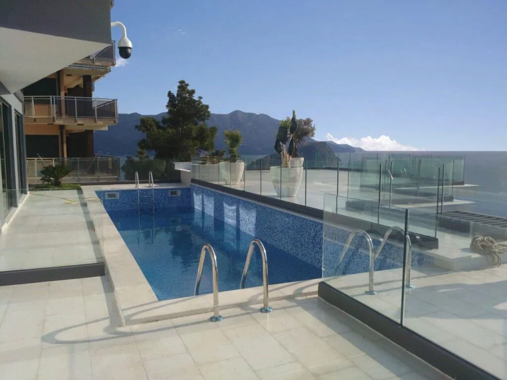 Outdoor swimming pool with blue mosaic tiles on a terrace overlooking the sea and mountains.