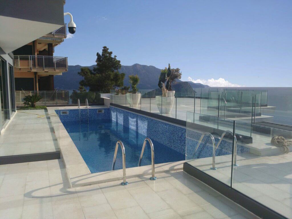 Open-air pool on the villa terrace in Budva, Montenegro, with panoramic sea and mountain views, glass railing.