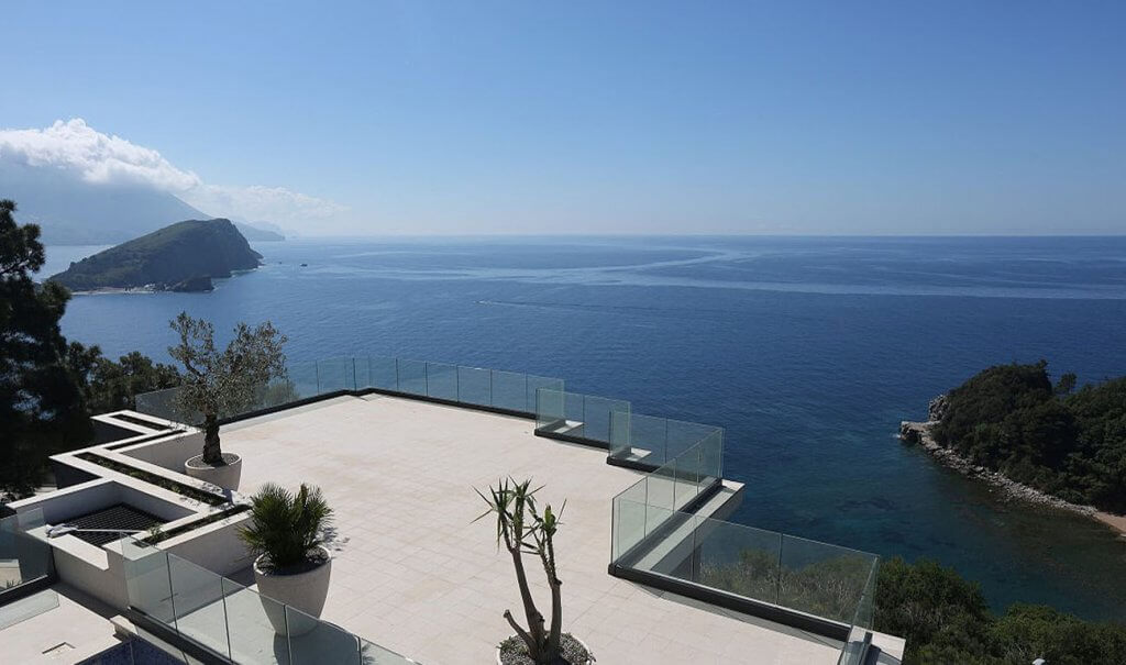 Panoramic villa terrace in Budva, Montenegro, with glass railing and views of the Adriatic Sea and an island.