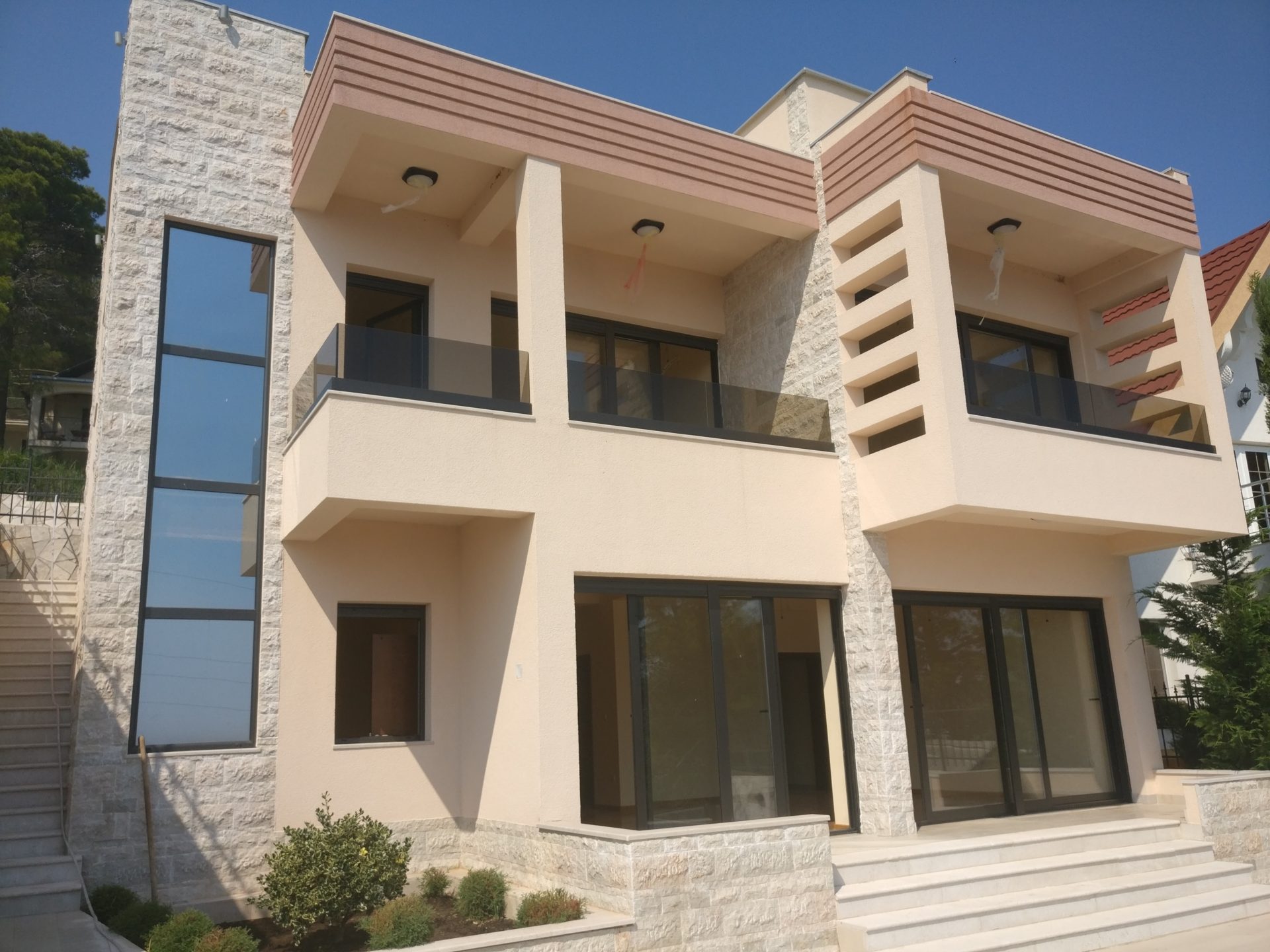 Modern two-story house in Shushan, Montenegro: panoramic windows, terraces with glass railings, and stone finishes.