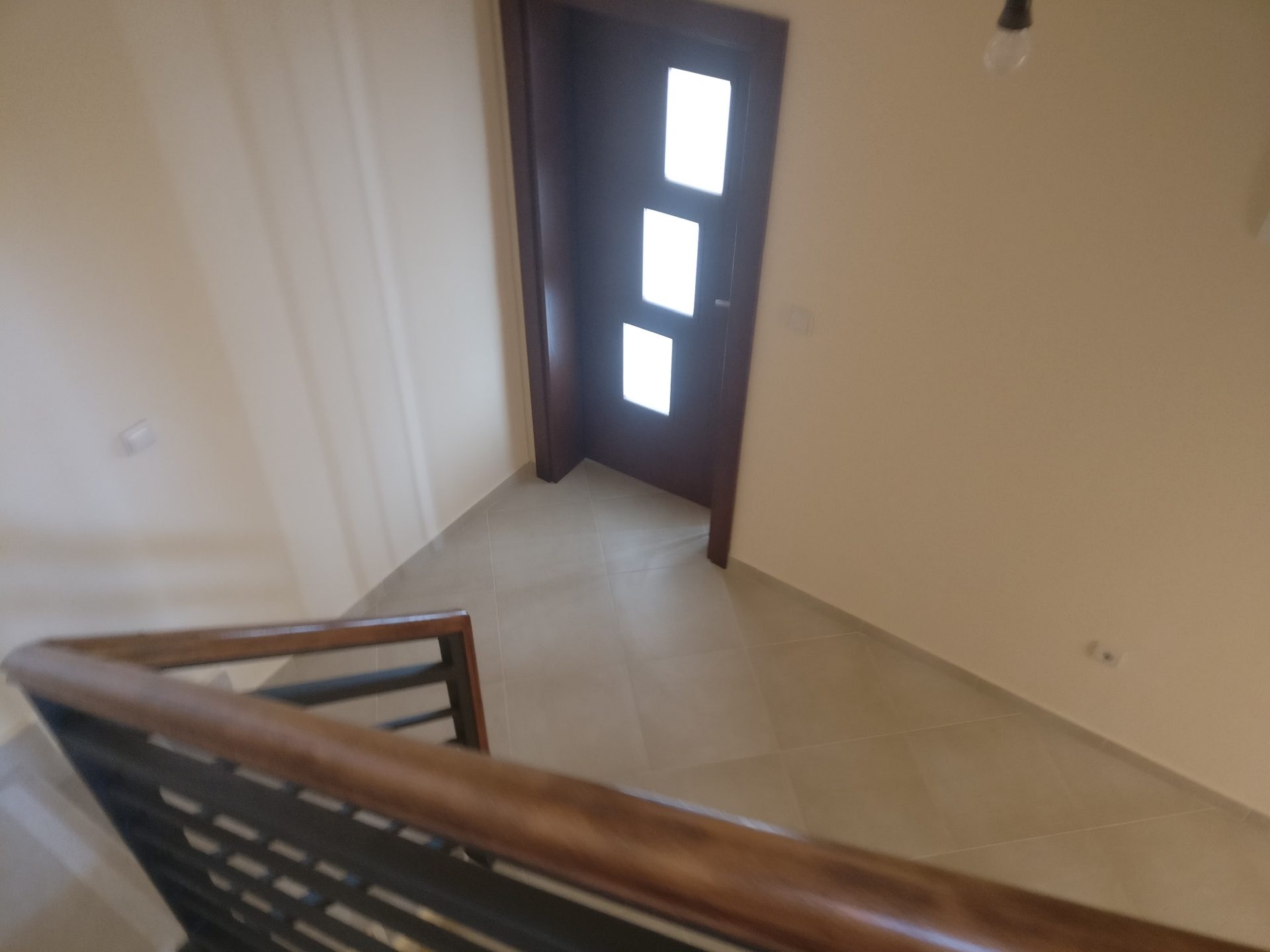 Top view of the staircase with wooden railings and the front door in the house, Shushan, Montenegro. Light tile and finishes.
