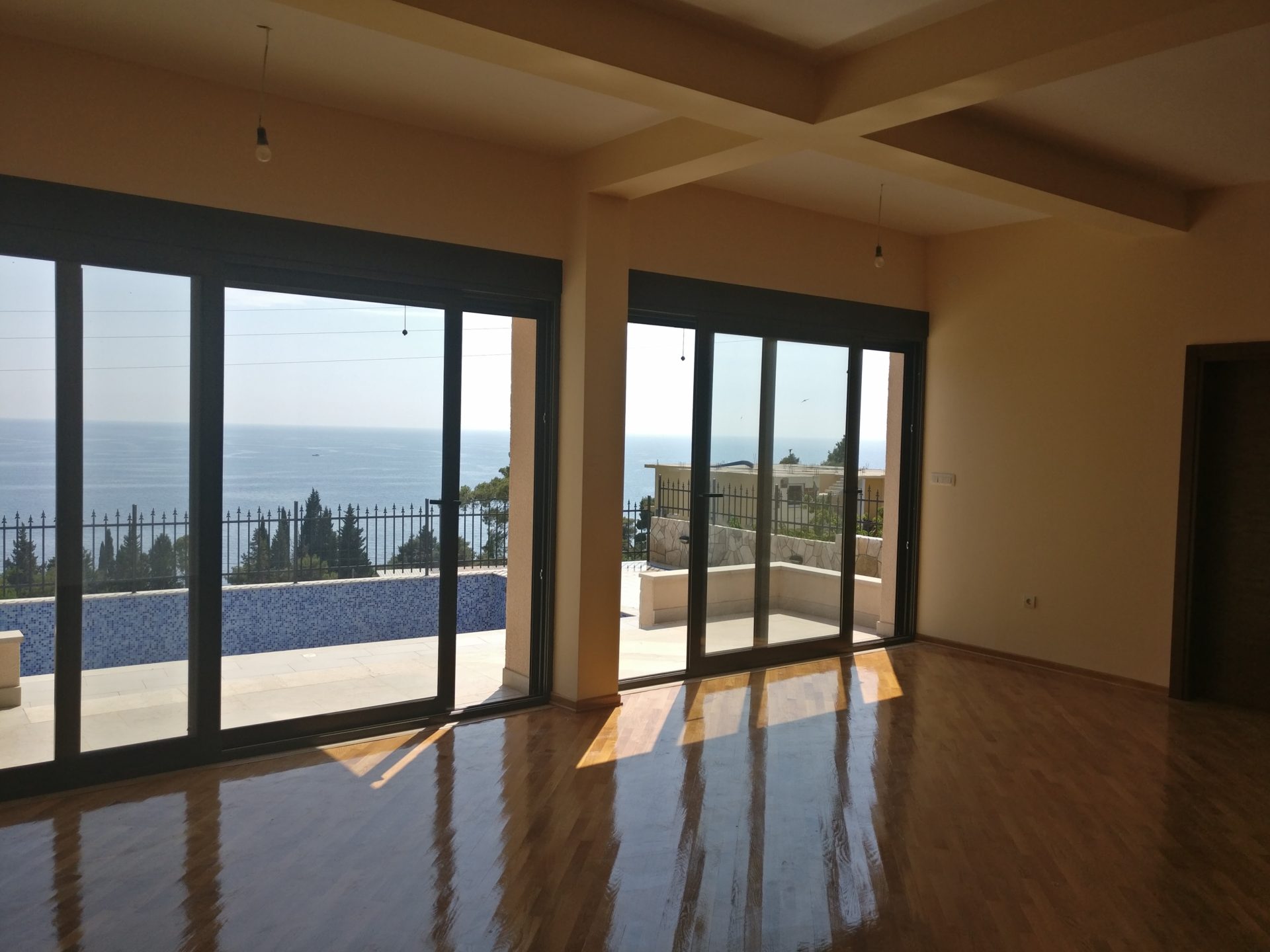 Living room in a house in Shushan, Montenegro: panoramic windows, sea view and terrace with a pool, parquet flooring.