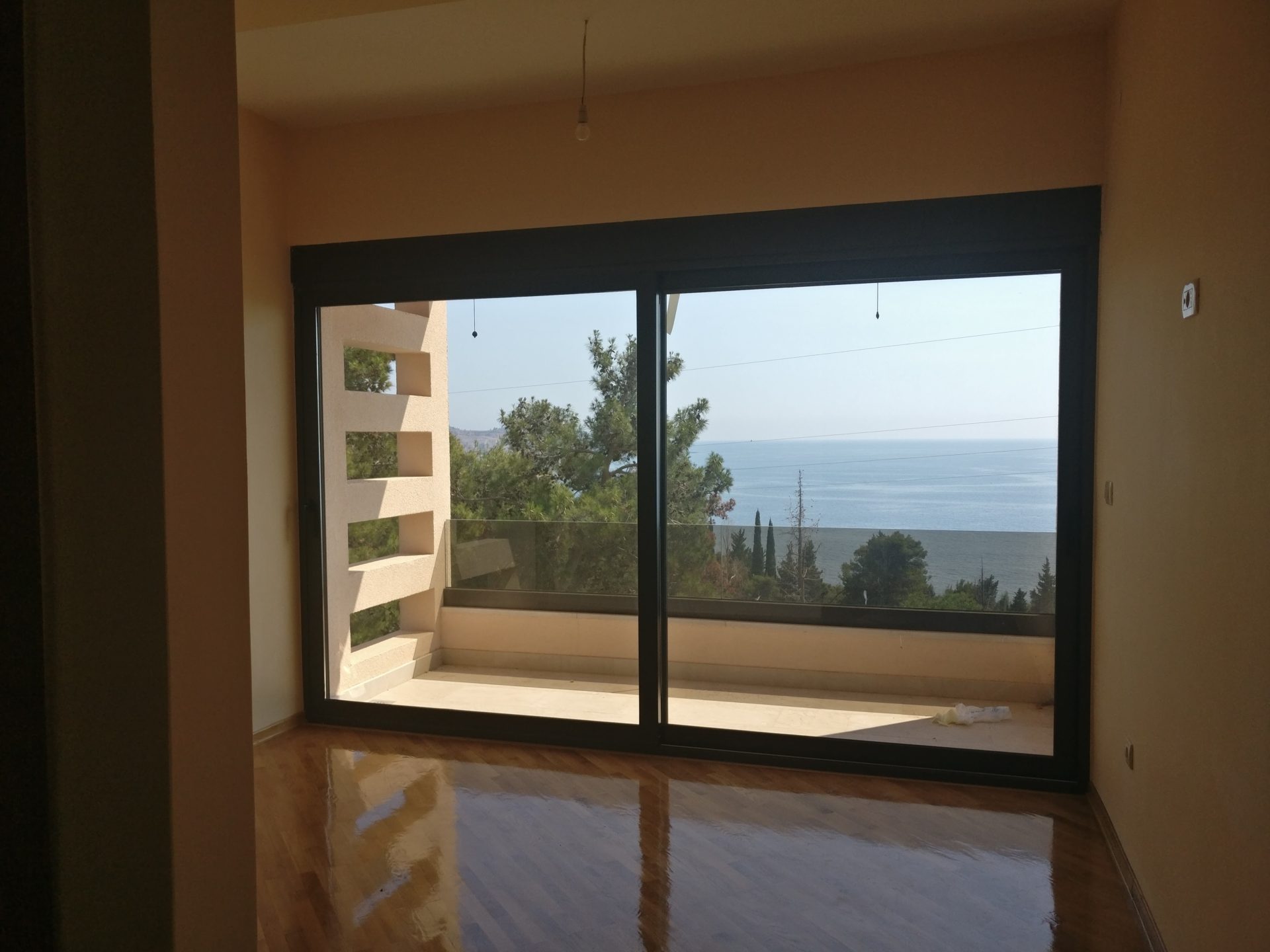 Living room with a panoramic window and sea view in a house, Shushan, Montenegro: parquet flooring and access to the terrace.