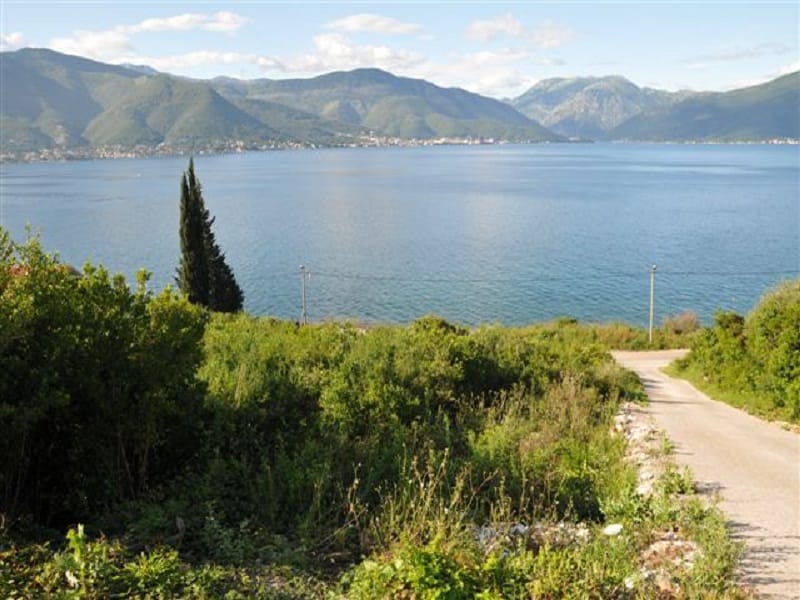 Land plot in Krašići, Montenegro: panoramic sea and mountain views with access road and greenery.