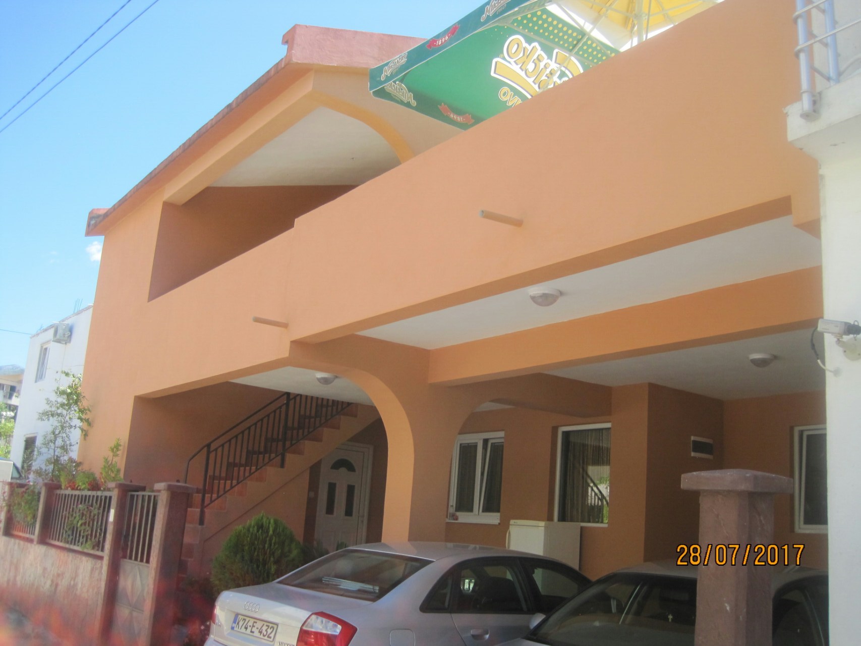 Two-story house with terraces and parking in Shushan, Montenegro: building facade with an exterior staircase and cars.