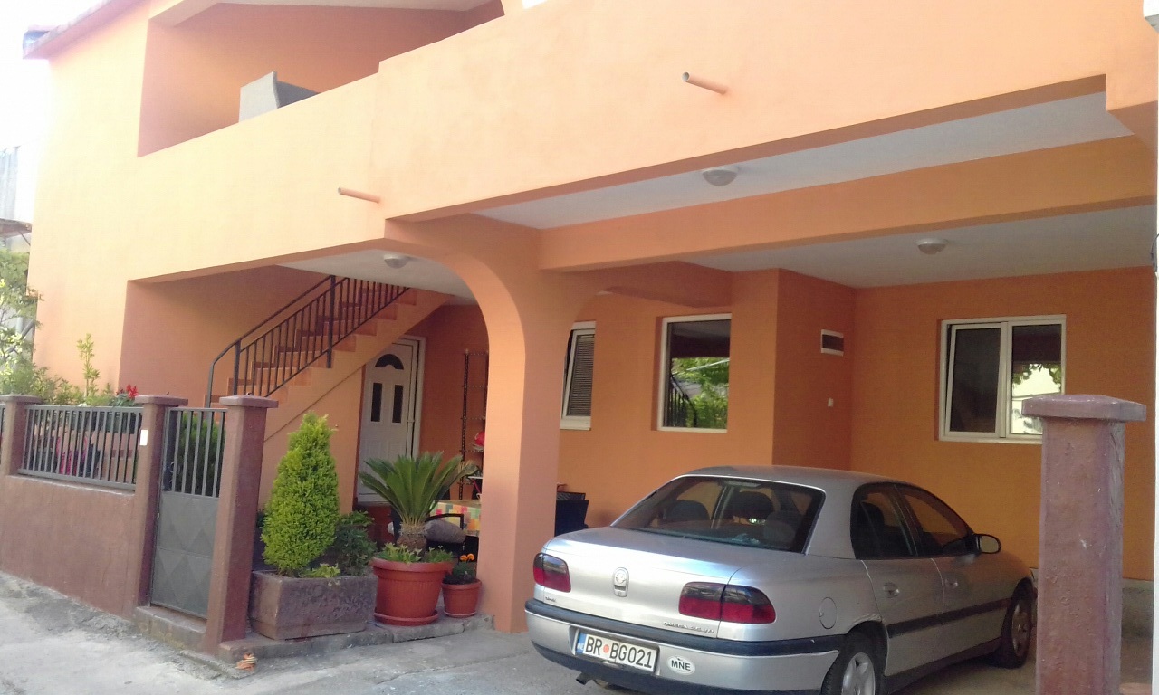 Two-story house in Shushan, Montenegro: orange facade, covered parking for cars, and an exterior staircase.