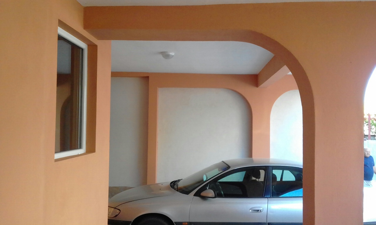 Covered parking with arched openings by the house in Shushan, Montenegro: view of the carport and building facade.