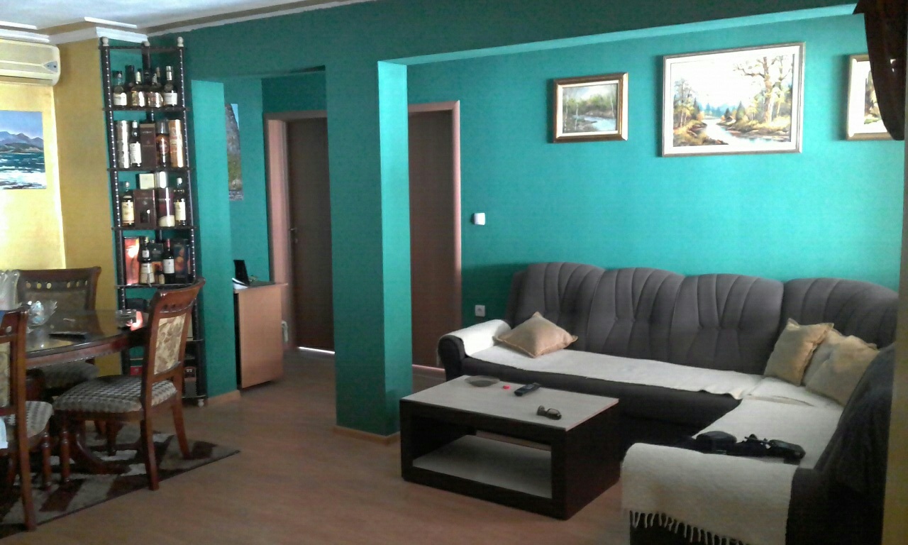 Living room with turquoise walls, an L-shaped sofa, and a dining area in a house, Shushan, Montenegro.