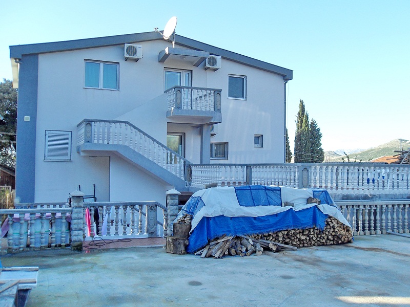 Two-story house with an exterior staircase and terrace in Dobri Vody, Montenegro: front view with firewood and balustrade.