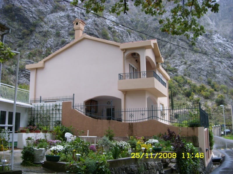 Two-story house in Orahovac, Montenegro, with a balcony, terrace, and a well-kept garden against a backdrop of rocky mountains.