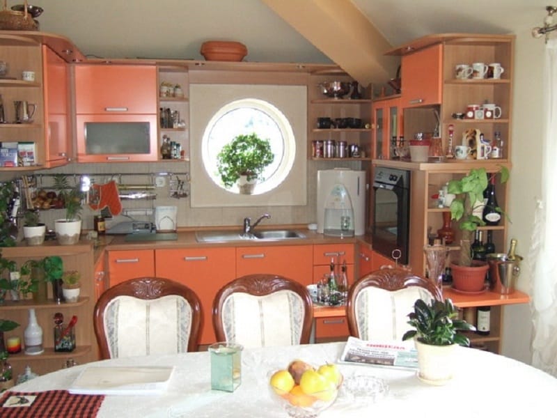 Cozy kitchen with an orange cabinet set and a round window in the house, Orahovac, Montenegro. Dining area with classic chairs.