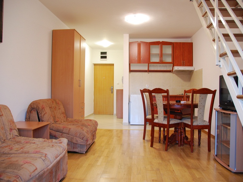 Living room with kitchen and staircase in an apartment in Bečići, Montenegro: wooden furniture, dining area, and bright interior.