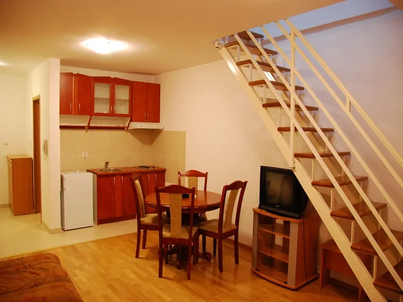 Kitchen area with wooden cabinets, dining table, and staircase leading to the upper floor in an open plan.
