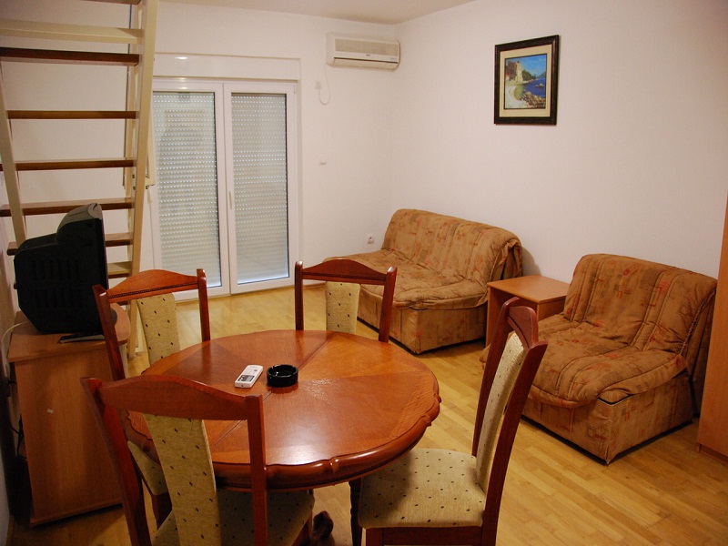 Living room in an apartment in Bečići, Montenegro: dining area, soft seating, staircase to the second level, and access to the balcony.
