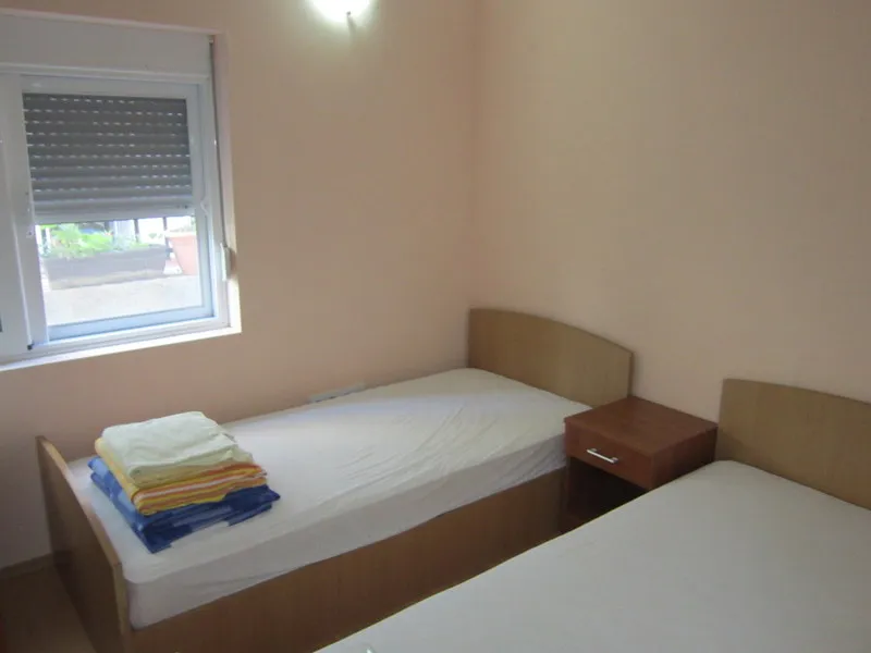 Two single beds with white linens and a wooden nightstand positioned next to a window.
