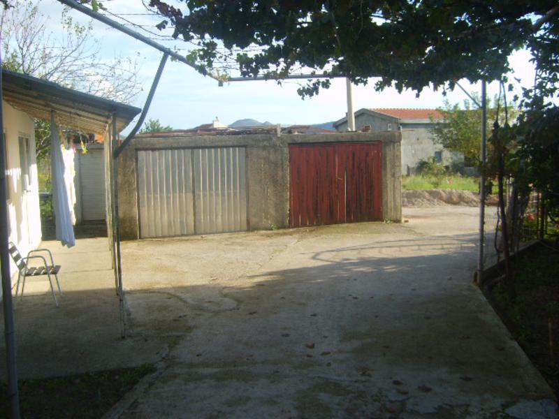 Courtyard of a private house in Shushan, Montenegro: concrete площадка, garage with a gate, and a canopy with grapevines.