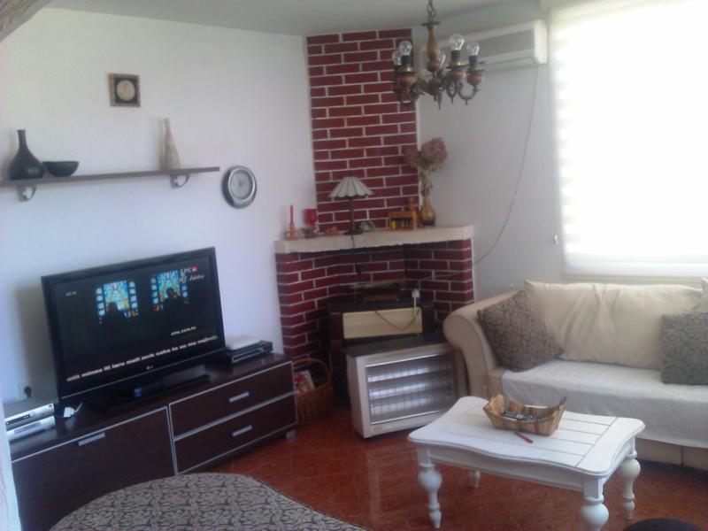 Living room in a house in Shushan, Montenegro: a bright room with a corner red brick fireplace, sofa, and TV area.