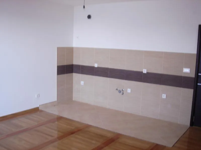 Empty room with wooden flooring and a tiled wall section featuring water pipes and electrical outlets.